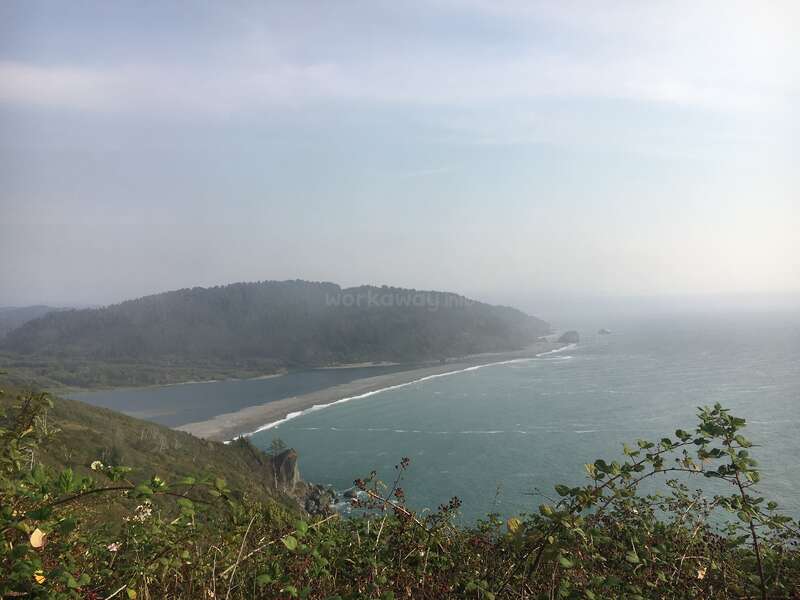The image depicts a serene coastal scene with a misty sky, featuring a body of water, a sandy beach, and lush greenery in the foreground.