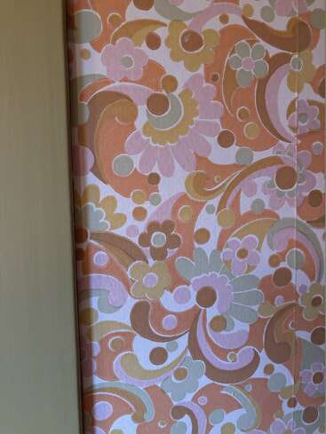 Dieses Bild zeigt eine Retro-Tapete mit einem auffälligen Blumenmuster in Orange-, Rosa-, Gelb- und Grüntönen. Das Design besteht aus Wirbeln, Kreisen und Blumen.