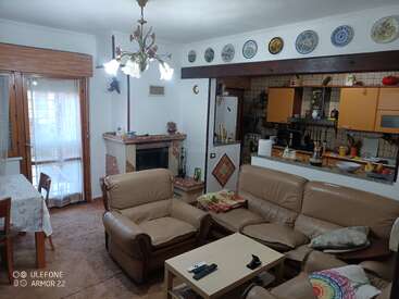 Este acogedor salón cuenta con sofás de cuero beige, una chimenea, una mesa de comedor y una cocina abierta. La pared sobre la cocina está decorada con platos.