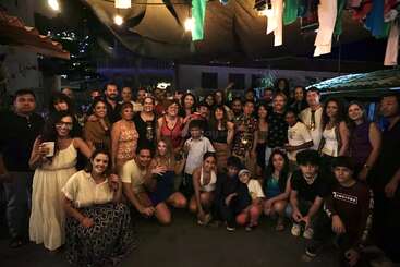 A large group of people, adults and children, gather together at night under string lights, smiling and posing for a celebration or party, creating a joyful atmosphere.