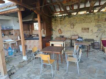 Cette cuisine d'extérieur au charme rustique se caractérise par un sol en pierre, des poutres apparentes, des tables et des chaises simples, un plan de travail carrelé, des murs en pierre et un charme vintage et champêtre omniprésent.
