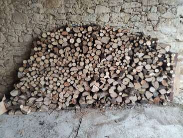 Un tas de bois de chauffage soigneusement empilé repose contre un mur de pierre rustique dans un coin abrité, prêt à être utilisé pendant les mois d'hiver à venir.