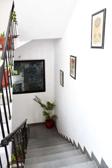 La imagen muestra una escalera blanca con barandillas negras, plantas en macetas y obras de arte enmarcadas en las paredes, que crean un ambiente limpio y elegante.