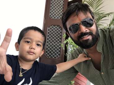 La imagen muestra a un hombre y un niño posando para un selfie, con el niño haciendo un signo de la paz y el hombre con gafas de sol.