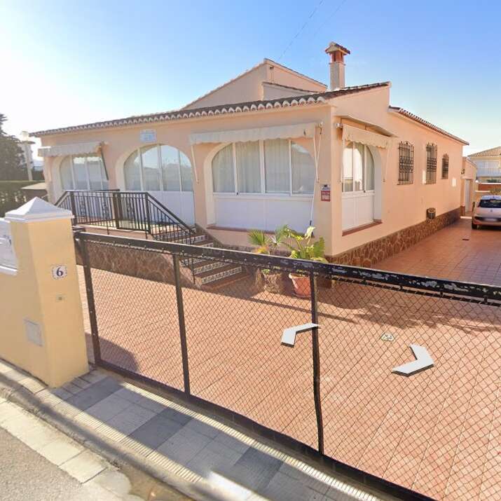 The image shows a single-story house with a tiled roof, enclosed terrace, black metal fence, large driveway, potted plants, and a parked car outside.