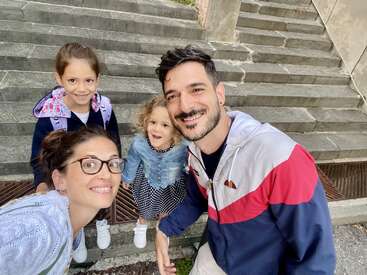 Une famille heureuse de quatre personnes sourit pour un selfie en plein air. Ils se tiennent ensemble près de marches en pierre, habillés de façon décontractée, l'air joyeux et profitant du temps passé ensemble.