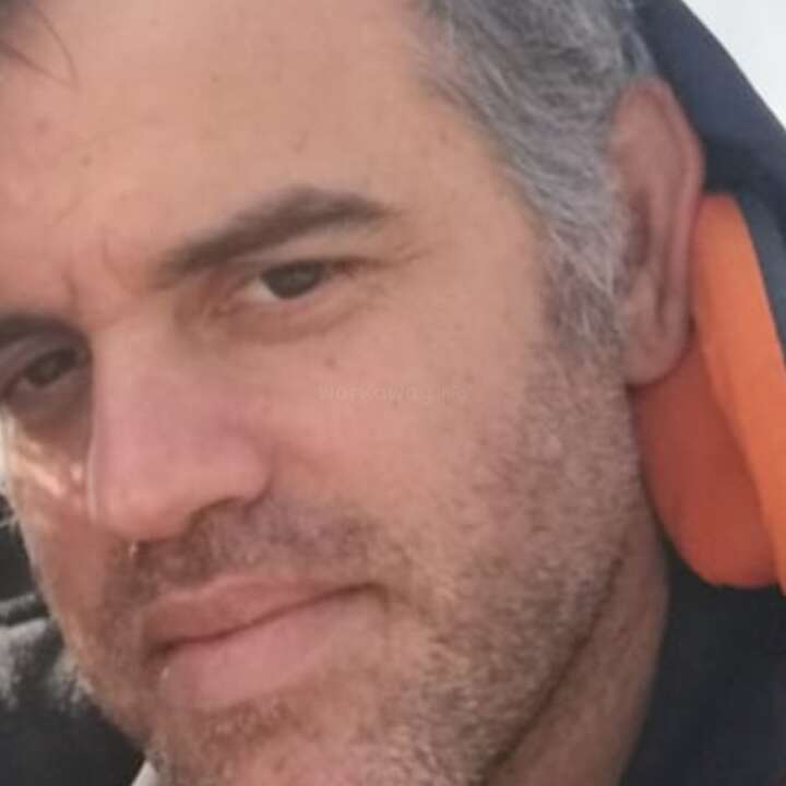 L'image est un gros plan du visage d'un homme, avec un sweat à capuche noir et orange, doté d'une fermeture éclair et d'un texte, sur un fond blanc.