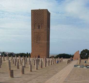 This image shows the Hassan Tower in Rabat, Morocco, surrounded by numerous stone columns and a spacious plaza under a partly cloudy blue sky.