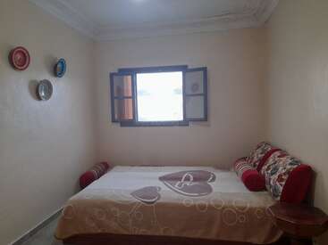 This is a simple, cozy bedroom with a double bed, heart-patterned blanket, three wall decorations, open window, and decorative red and floral pillow accents.