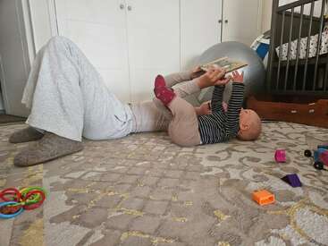 Un parent et son bébé sont allongés sur le tapis, partageant un livre. Des jouets sont éparpillés, créant une scène douillette et ludique dans une chambre d'enfant.