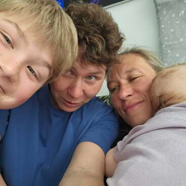 A heartwarming selfie of a smiling family: a boy, two adults, and a baby cuddling together, radiating love, joy, and togetherness in a cozy setting.