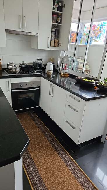 Cuisine moderne avec armoires blanches, comptoirs noirs, cuisinière à gaz, four, ustensiles divers, grille-pain, bouilloire, vaisselle, coupe de fruits, plantes d'intérieur et tapis à motifs. Espace lumineux.