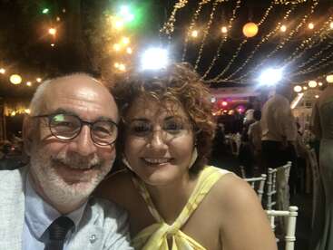 Un couple souriant prend un selfie lors d'un événement festif, entouré de lumières et de décorations suspendues, créant une atmosphère joyeuse, chaleureuse et festive la nuit.