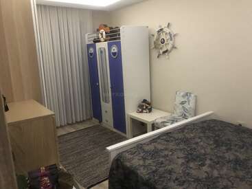 Cette chambre confortable comprend une armoire bleue, une décoration murale nautique, un petit bureau, une chaise à motifs, un lit avec une literie foncée, une commode, un tapis et des rideaux clairs.