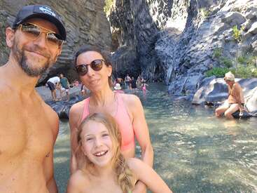 Une famille souriante profite d'une journée ensoleillée dans les gorges d'une rivière rocheuse. Les gens se baignent et se détendent, entourés de falaises impressionnantes et d'une eau claire et peu profonde dans la nature.