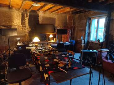 A cozy, rustic music studio with exposed stone walls, wooden ceiling beams, and warm lighting. Various instruments, microphones, and audio equipment fill the cluttered, creative space.