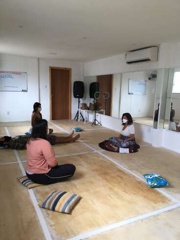 The image depicts a serene room with four women seated on the floor, surrounded by mirrors and a whiteboard, exuding a sense of calm and tranquility.
