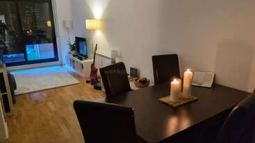 Ein gemütlicher Wohn- und Essbereich mit Holzböden, Kerzen auf dem Tisch, modernen Möbeln, einer Gitarre, Fernseher, Lampen und blauer Akzentbeleuchtung in der Nähe des Balkons.