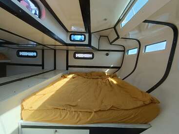 L'image représente l'intérieur d'un camping-car, avec un lit aux draps jaunes, des fenêtres et un plafond blanc, mettant en valeur un espace de vie confortable et compact.