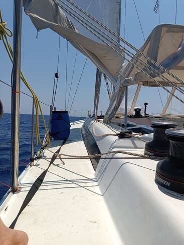 L'image représente un voilier sur l'eau, avec une coque blanche et un ciel bleu en arrière-plan. Le bateau est équipé de cordes et d'un mât.