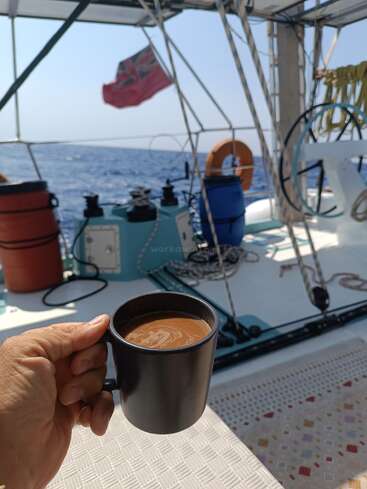 L'image représente une scène sereine d'une personne sirotant un café sur un bateau, avec l'océan et le ciel visibles en arrière-plan.
