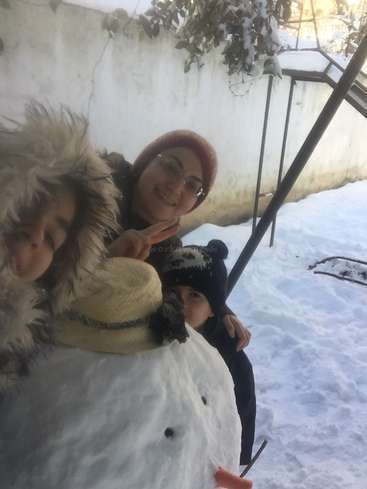 Das Bild zeigt eine Frau und zwei Kinder, die für ein Foto im Schnee posieren, mit einem großen Schneemann im Vordergrund. Die Frau trägt eine rote Mütze.