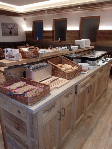 This cozy buffet features wooden cabinets, baskets of bread and rolls, a toaster, plates, eggs, and hot trays in a rustic dining setting.