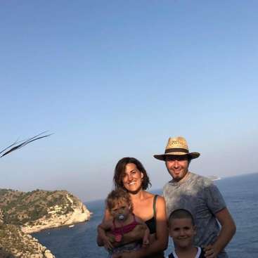Das Bild zeigt eine vierköpfige Familie, die für ein Foto auf einer Klippe mit Blick auf den Ozean posiert, mit einem klaren blauen Himmel im Hintergrund.