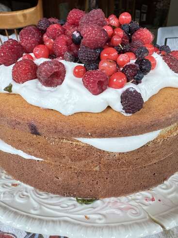 Ein selbstgebackener Schichtkuchen, garniert mit Schlagsahne und einer großzügigen Mischung aus frischen Himbeeren, Brombeeren, Johannisbeeren und Heidelbeeren, serviert auf einem dekorativen Teller.