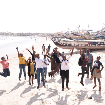 L'image représente un groupe de personnes sautant sur une plage de sable avec des bateaux à l'arrière-plan, transmettant un sentiment de joie et de célébration.