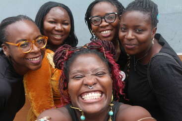 Cinco mujeres están muy juntas, sonriendo alegremente para hacerse un selfie. Sus expresiones irradian felicidad y amistad, capturando un momento animado, positivo y despreocupado juntas.