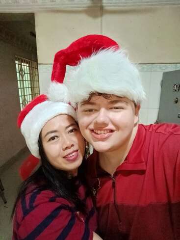 Un hombre y una mujer sonrientes con gorros de Papá Noel posan juntos para una selfie. Ambos van vestidos de rojo, creando un ambiente festivo y alegre en el interior.