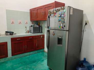 Esta cozinha tem armários de madeira vermelhos, uma geladeira prateada decorada com ímãs, um forno de micro-ondas, backsplash de azulejos verdes, piso turquesa e um bebedouro. Espaço aconchegante.