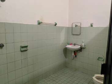 Um banheiro simples com azulejos verdes claros, pia na parede, espelho pequeno, porta-sabonete, porta-toalhas, vaso sanitário e produtos de higiene pessoal básicos; aparência minimalista e um pouco ultrapassada.