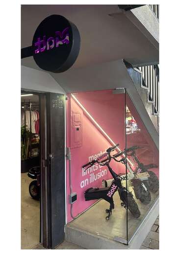 En un escaparate hay un cartel negro con el logotipo morado, un expositor de cristal con dos bicicletas y una pared rosa que dice: "los límites mentales son una ilusión".