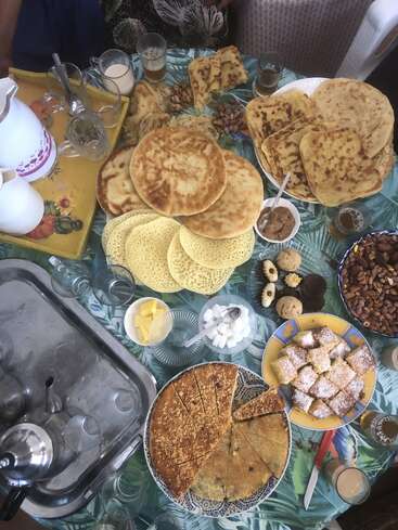Ein bunter Tisch mit marokkanischen Broten, Pfannkuchen, Gebäck, Nüssen, Teegläsern, Zucker, Butter und Teekannen schafft eine festliche, traditionelle Frühstücksatmosphäre.