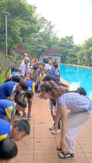 Eine Gruppe von Kindern und Erwachsenen nimmt an einer Outdoor-Aktivität in der Nähe eines Pools teil. Sie beugen sich in Reihen und genießen einen lustigen, energiegeladenen und spielerischen Moment.