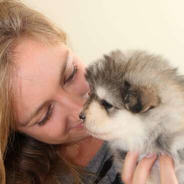 A woman lovingly holds a fluffy, young puppy close to her face, smiling softly. The puppy gazes back, highlighting a tender moment of affection and connection.