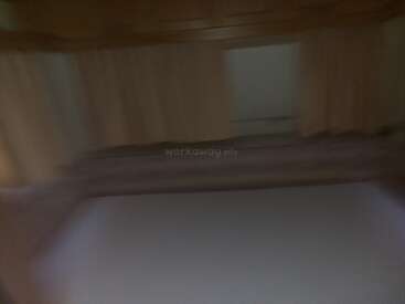 This image is blurry and dimly lit. It appears to show a bed with beige curtains behind it, possibly in a camper or small room.