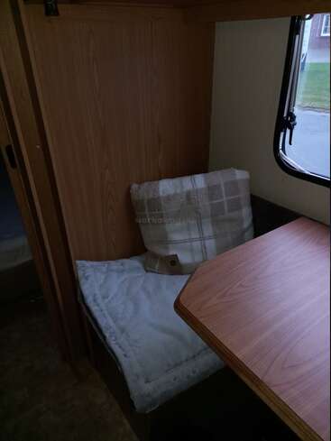 A cozy corner inside a camper or RV, featuring a padded seat with a plaid pillow, wooden table, window, and soft lighting creating a warm atmosphere.