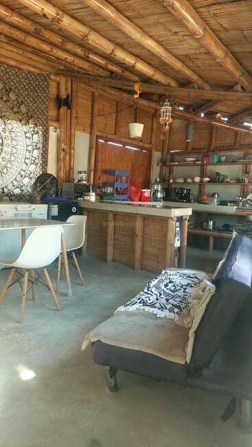 This cozy room features bamboo walls and ceiling, an eclectic kitchen, white chairs, a sofa with patterned blanket, open shelves, and a decorative tapestry.