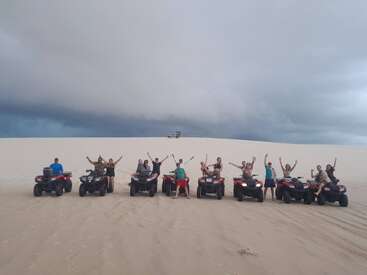 Un grupo de personas posa con entusiasmo en un quad en un desierto arenoso bajo un cielo nublado y espectacular, celebrando la aventura y la diversión en un paisaje abierto.