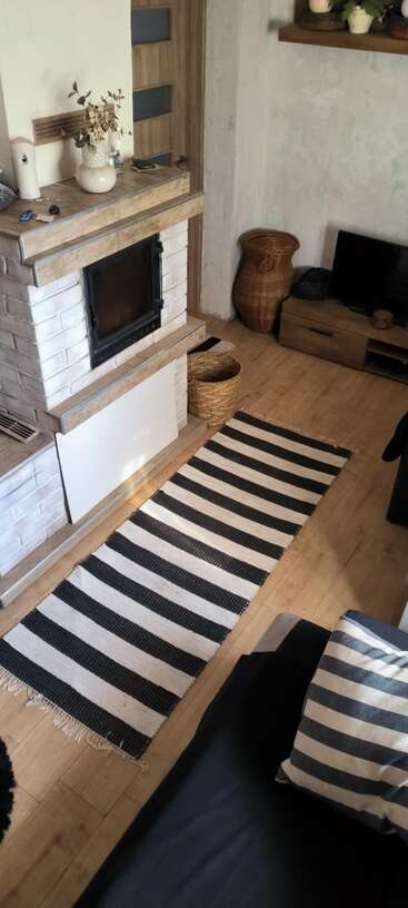 A cozy living room with a striped black-and-white rug, fireplace, wooden floor, striped pillow, TV stand, woven baskets, and decorative items creating a warm atmosphere.