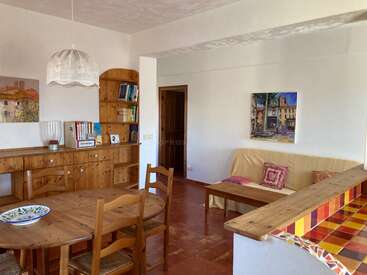 Este acogedor salón-comedor cuenta con muebles de madera, cojines de colores, cuadros, una estantería, una mesa de comedor redonda y azulejos brillantes y cálidos en la encimera de la cocina.