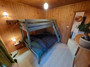 Esta acogedora habitación de madera cuenta con una moderna litera, plantas en macetas, lámparas de pared, una estantería y un ambiente suave y acogedor con una iluminación cálida.