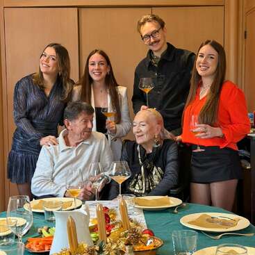 Une famille réunie autour d'une table de fête, souriante, un verre à la main, entourée de décorations de Noël et de petits en-cas, créant une ambiance chaleureuse et joyeuse, idéale pour faire la fête et passer un moment ensemble.