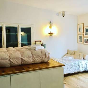 Das Bild zeigt ein ruhiges Schlafzimmer mit einem Bett, einer Liege und einem Fenster, das ein Gefühl der Ruhe und Gelassenheit ausstrahlt. Der Raum ist gut beleuchtet und einladend.