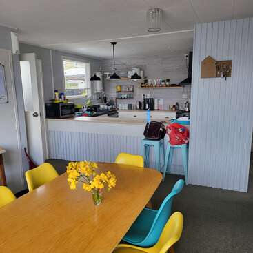 Uma cozinha aconchegante e uma área de jantar com mesa de madeira, cadeiras coloridas, centro de mesa com flores amarelas, banquetas azuis claras e eletrodomésticos modernos. Ambiente luminoso e convidativo.
