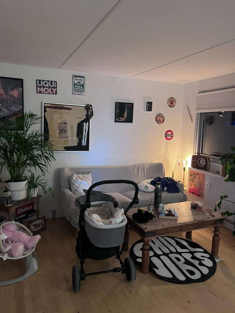 A cozy living room with a sofa, baby stroller, plants, wall art, retro decor, a wooden coffee table, and a round rug saying “CHILL VIBES.”