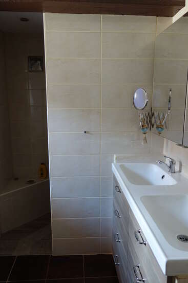 Cette photo montre une salle de bains comprenant un coin douche, des murs carrelés de couleur beige, un lavabo blanc avec des tiroirs, un miroir et un petit miroir de maquillage rabattable.